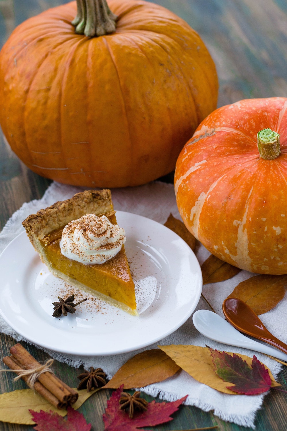 slice of pumpkin pie on a white plate in front of a couple of pumpkins