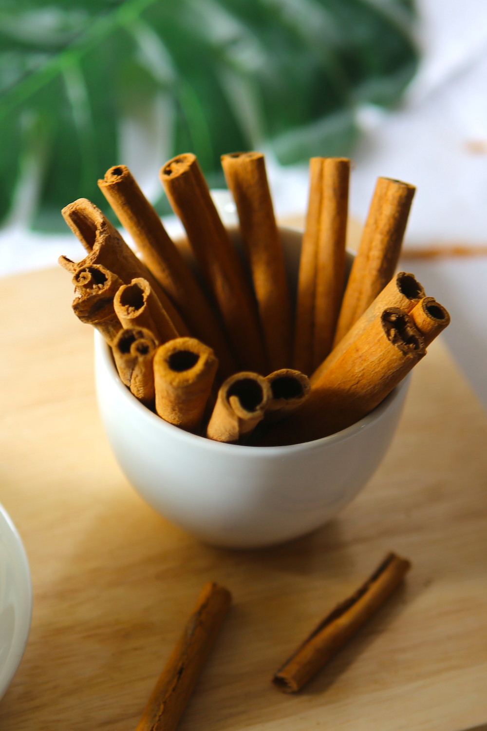 cinnamon sticks in a white cup on a wooden platter with a few scattered cinnamon sticks next to the cup
