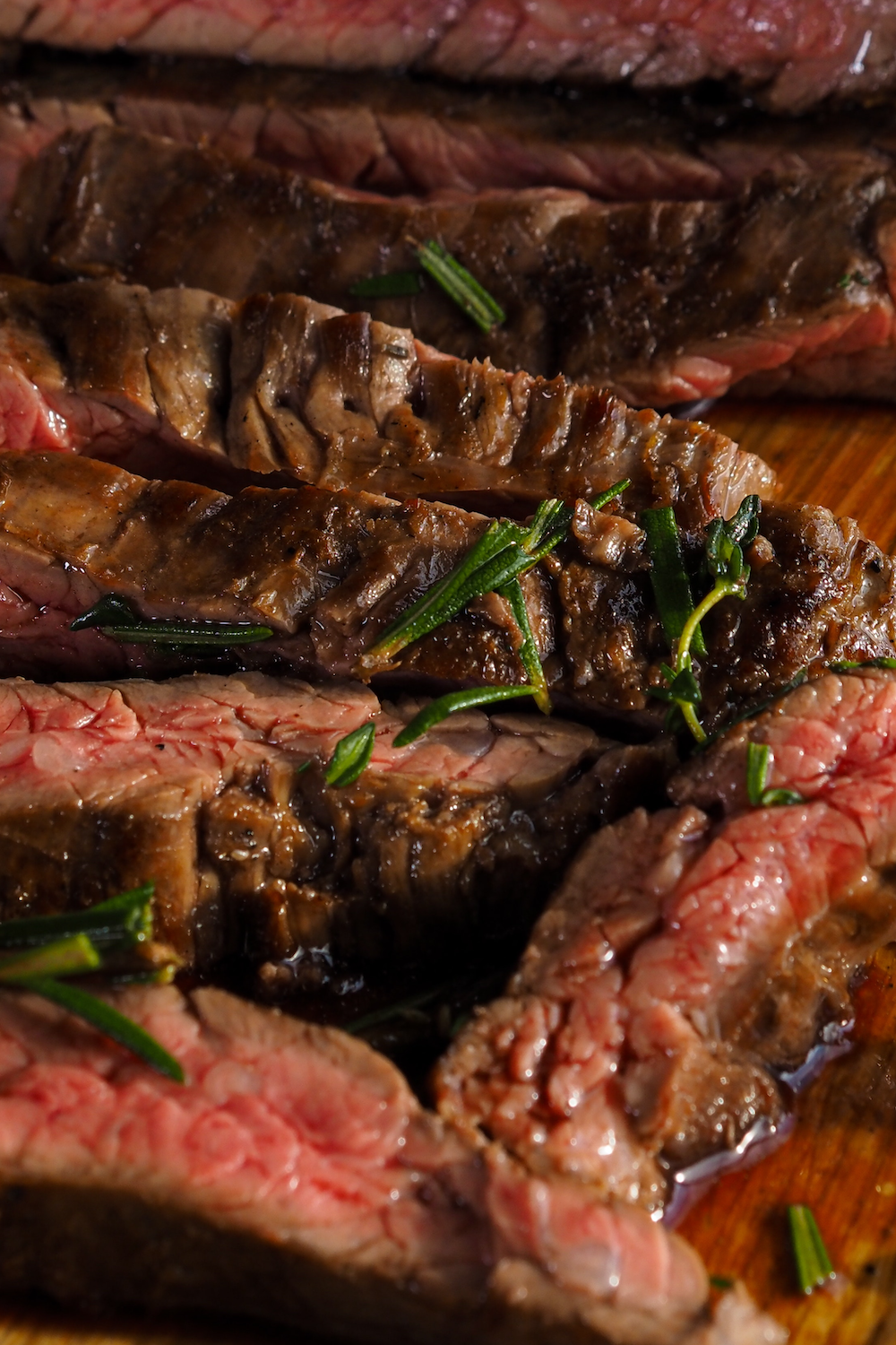 recipes for New York strip steak image showing juicy medium cooked slices of New York strip steak sprinkled with rosemary on a wooden cutting board