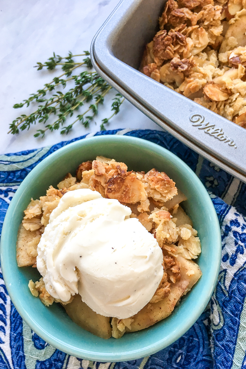 bowl of apple crisp topped with vanilla ice cream in bowl next to a pan of gluten free apple crisp