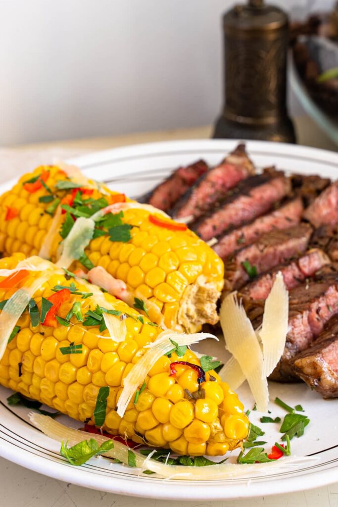 Sliced grilled balsamic marinated steak slices on a plate with two grilled corn on the cob