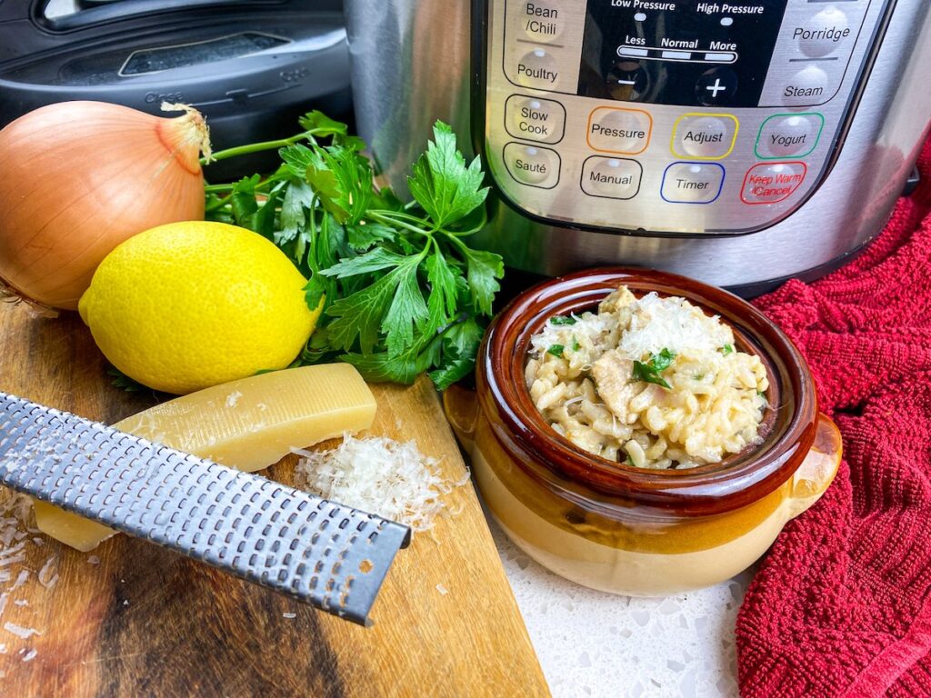 instant pot, bowl of lemon parsley chicken risotto, onion, lemon, fresh parsley, parmesan cheese and a cutting board