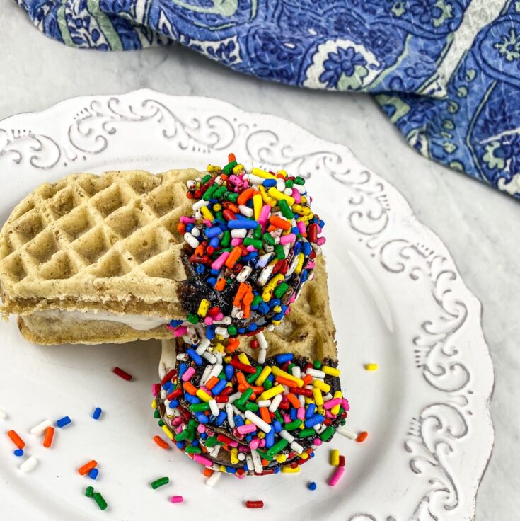 two waffle ice cream sandwiches with chocolate syrup and rainbow sprinkles