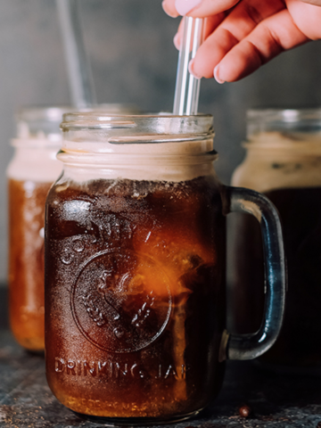 hand putting a straw into a mason jar of iced coffee