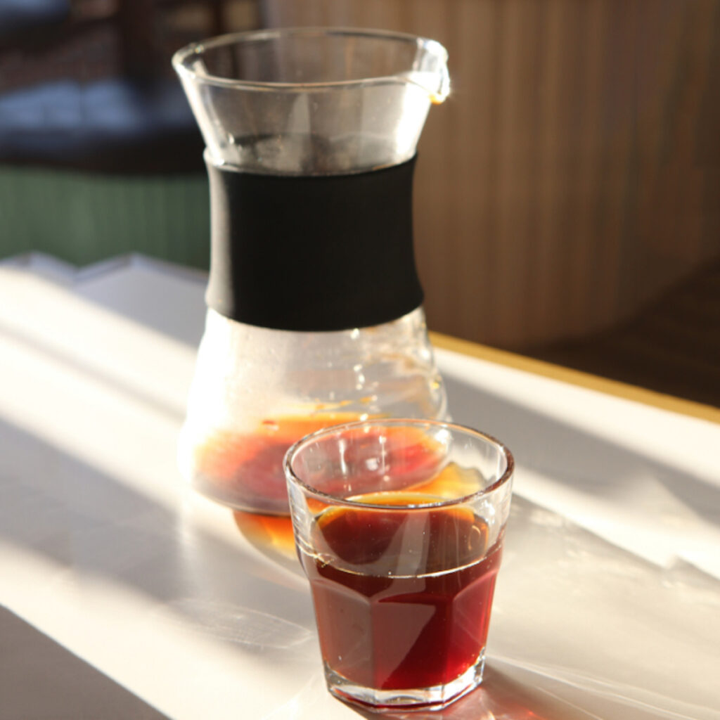 glass of coffee in front of a glass pitcher of cold brew coffee