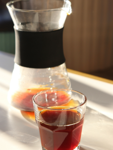 shot of coffee in a glass in front of a cold brew coffee pot