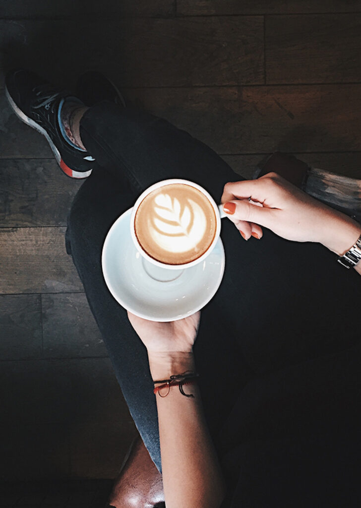 one hand holding a saucer and the other a cup of breve coffee