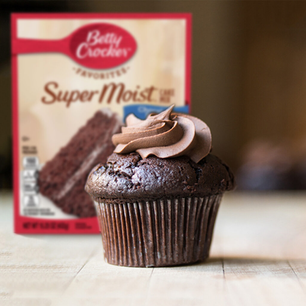 chocolate cupcake with chocolate frosting in front of a box of cake mix