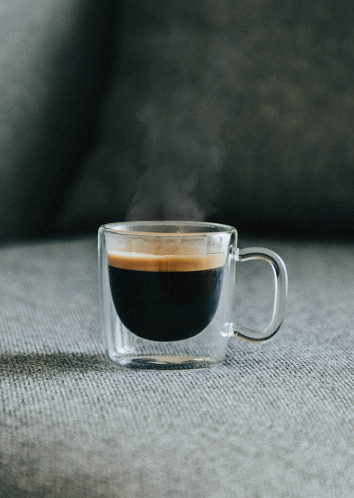 side view glass mug of steaming hot black coffee