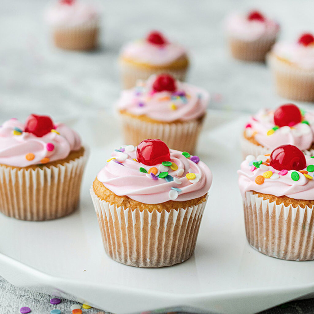 pink frosted cupcakes with cherries on top