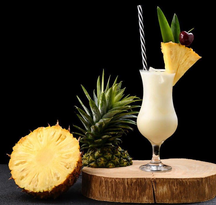 frozen pina colada from flavor portal recipe garnished with a pineapple wedge next to a sliced pineapple