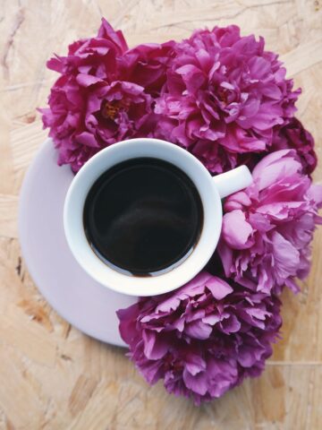 cup of coffee surrounded by pink flowers