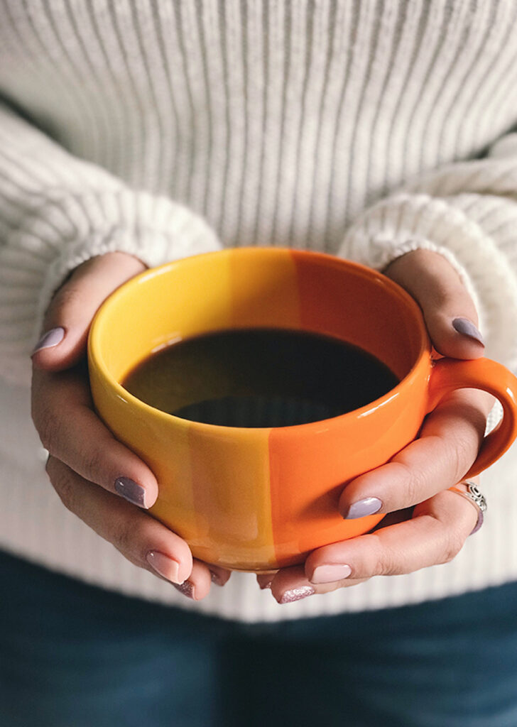 hands holding a bicolor yellow and orange coffee mug