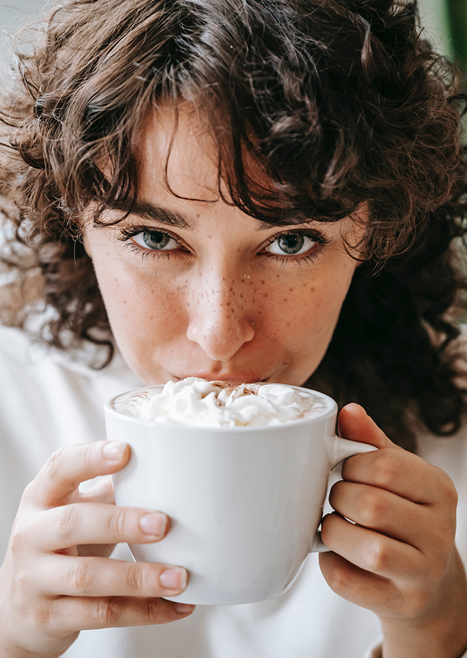 closeup of young woman sipping foam-covered coffee from a white cup