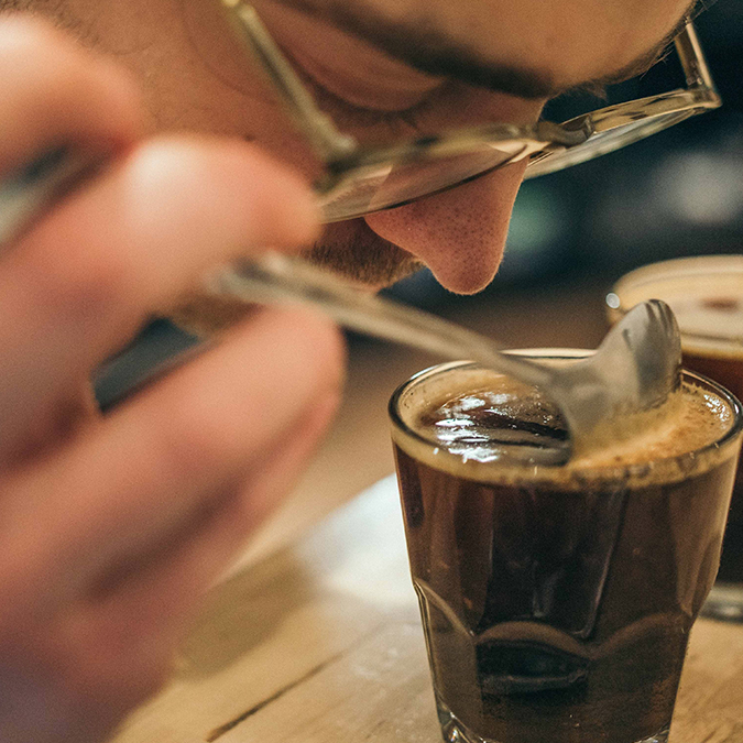 closeup of a man testing the aroma of a small cup of coffee in a glass
