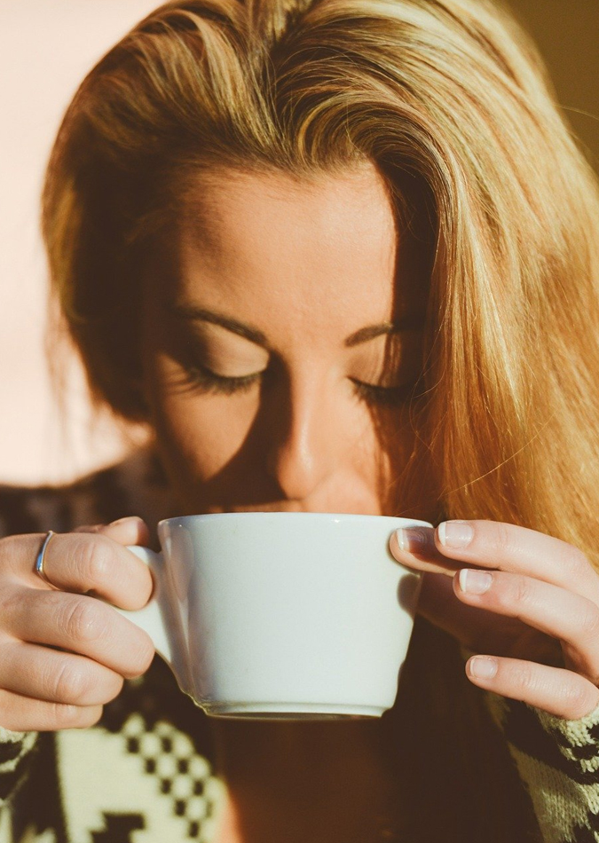 image of a woman in the morning light sipping coffee from a cup she's holding with both hands