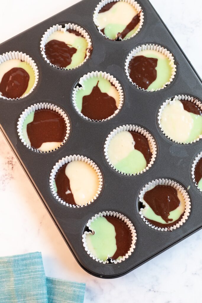 cupcake pan with cupcake liners filled with variegated green, brown and white cake mix for baking camouflage cupcakes