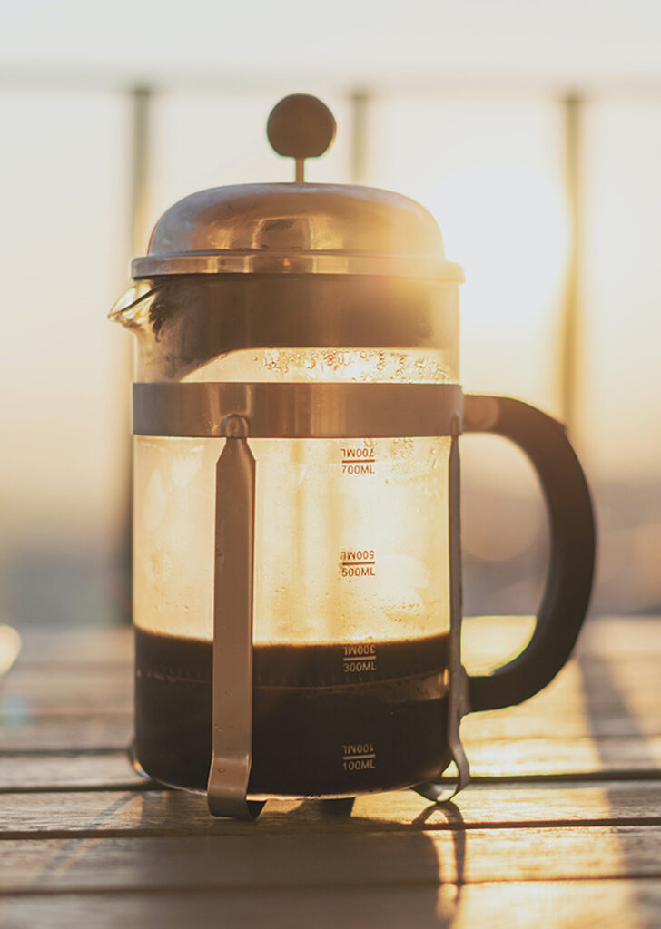 sun shining through a French press half filled with coffee