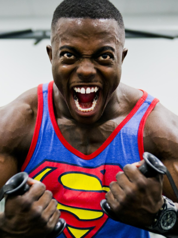 man wearing superman tank top flexing arms with dumb bells