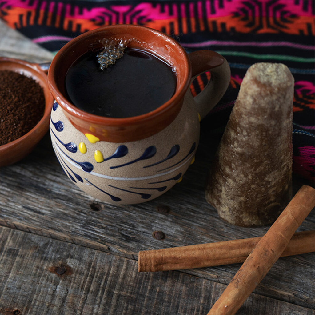 Mexican coffee in a traditionally decorated red ceramic mug with cafe de olla and cinnamon sticks beside it
