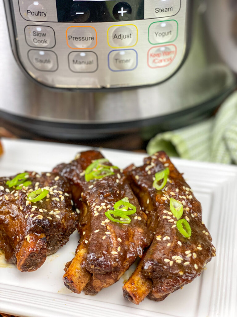 asian style sticky ribs on a white plate next to an Instant Pot