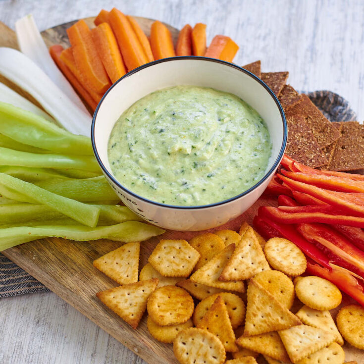 white bowl of zucchini dip surrounded by assorted cut fresh vegetables and crackers