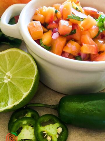 white bowl of spicy peach salsa next to sliced lime and jalapeno