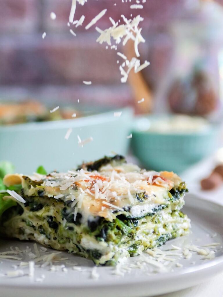 grated Parmesan cheese falling onto a slice of spinach broccoli lasagna