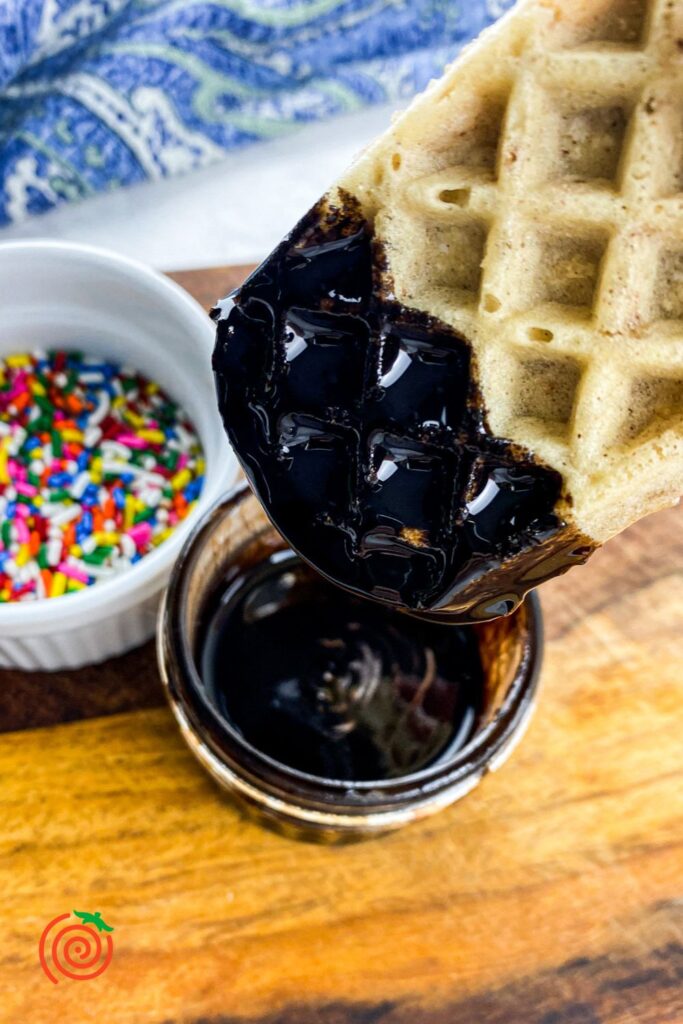 waffle ice cream sandwich dipped in chocolate syrup next to a bowl of rainbow sprinkles
