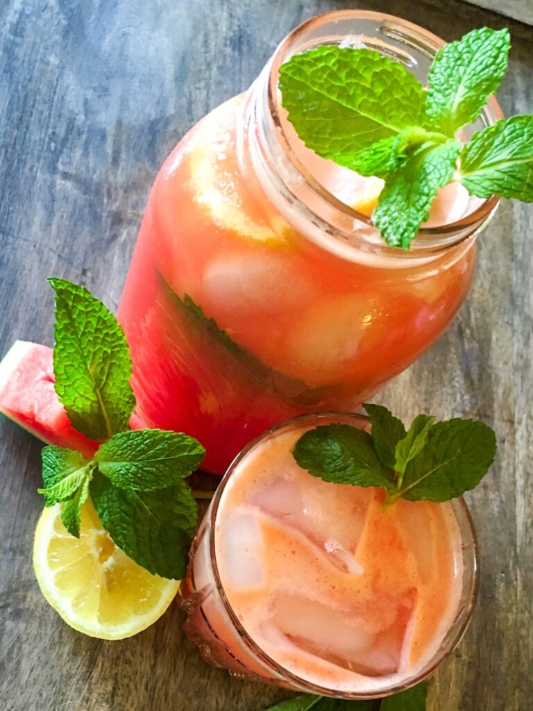 watermelon mint lemonade with a sprig of mint in a mason jar surrounded by fresh fruit