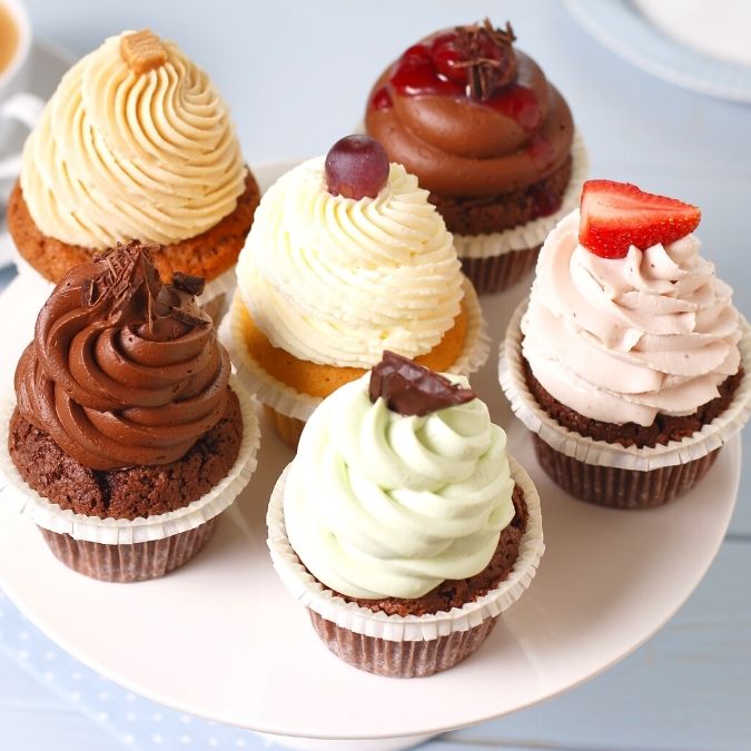 six different white and chocolate cupcakes each with different frosting and toppings on a plate