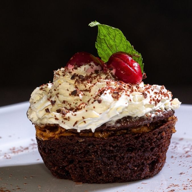 chocolate cupcake with buttercream frosting topped with cocoa powder, cherries and a mint leaf