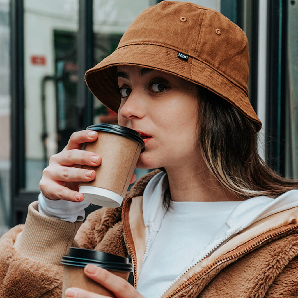 young woman with a brown hat sipping coffee from a paper cup