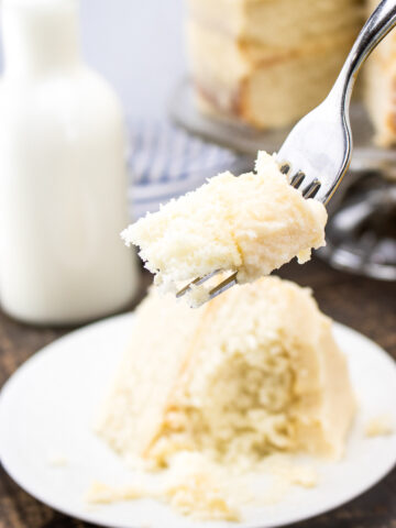closeup of a white layer cakeslice with buttercream frosting and a bite on the fork from a Flavor Portal recipe