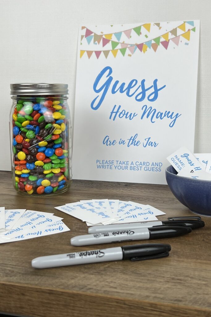 m&ms in a mason jar with Guess how many game sign and cards and pens for making guesses