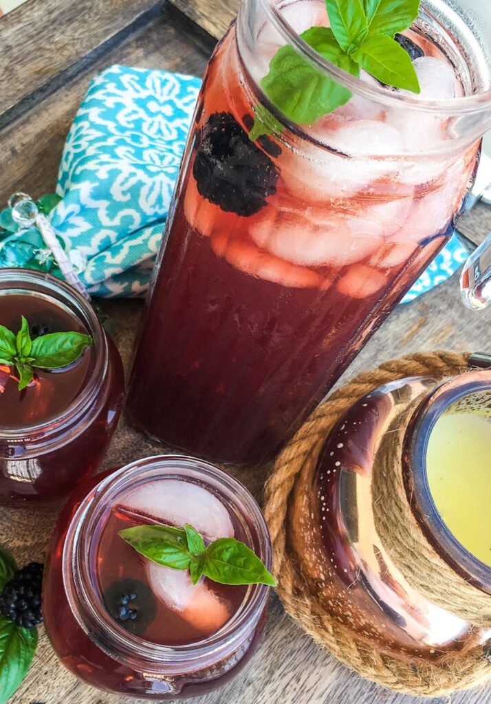 Tall pitcher with blackberry iced tea and two glasses garnished with basil