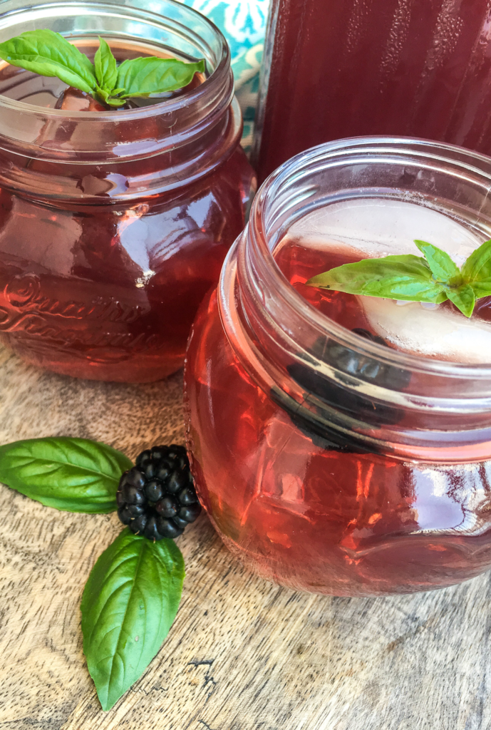Close up of mason jar glass with blackberry iced tea and garnishments 