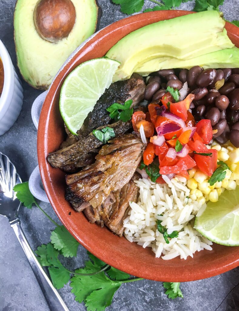 top view instant pot carnitas bowl from Flavor Portal recipe with avocado half and bowl of sauce
