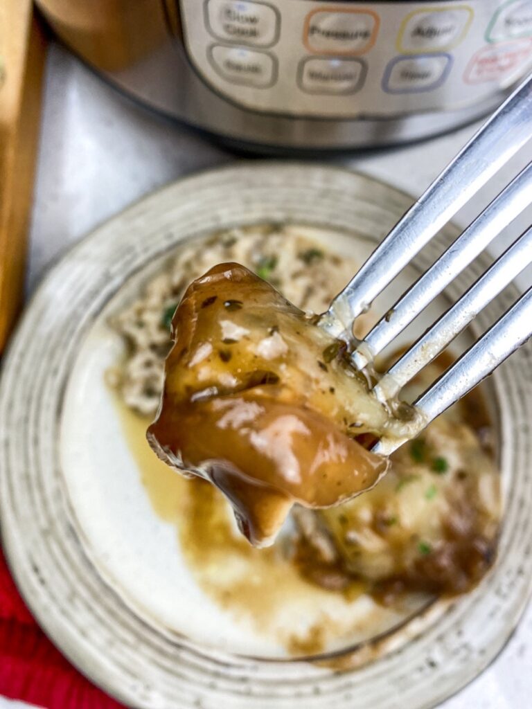 Piece of French onion chicken on a fork with white plate in background