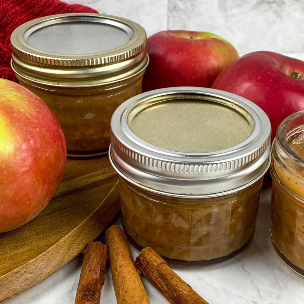 apple chutney jars next to an apple and cinnamon sticks