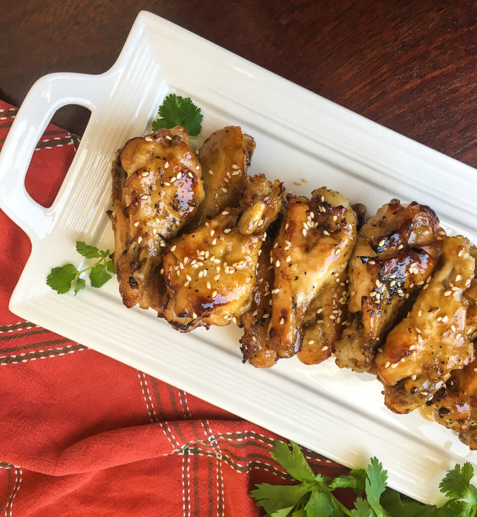Sesame garlic chicken wings on rectangular white plate garnished with cilantro for flavor portal