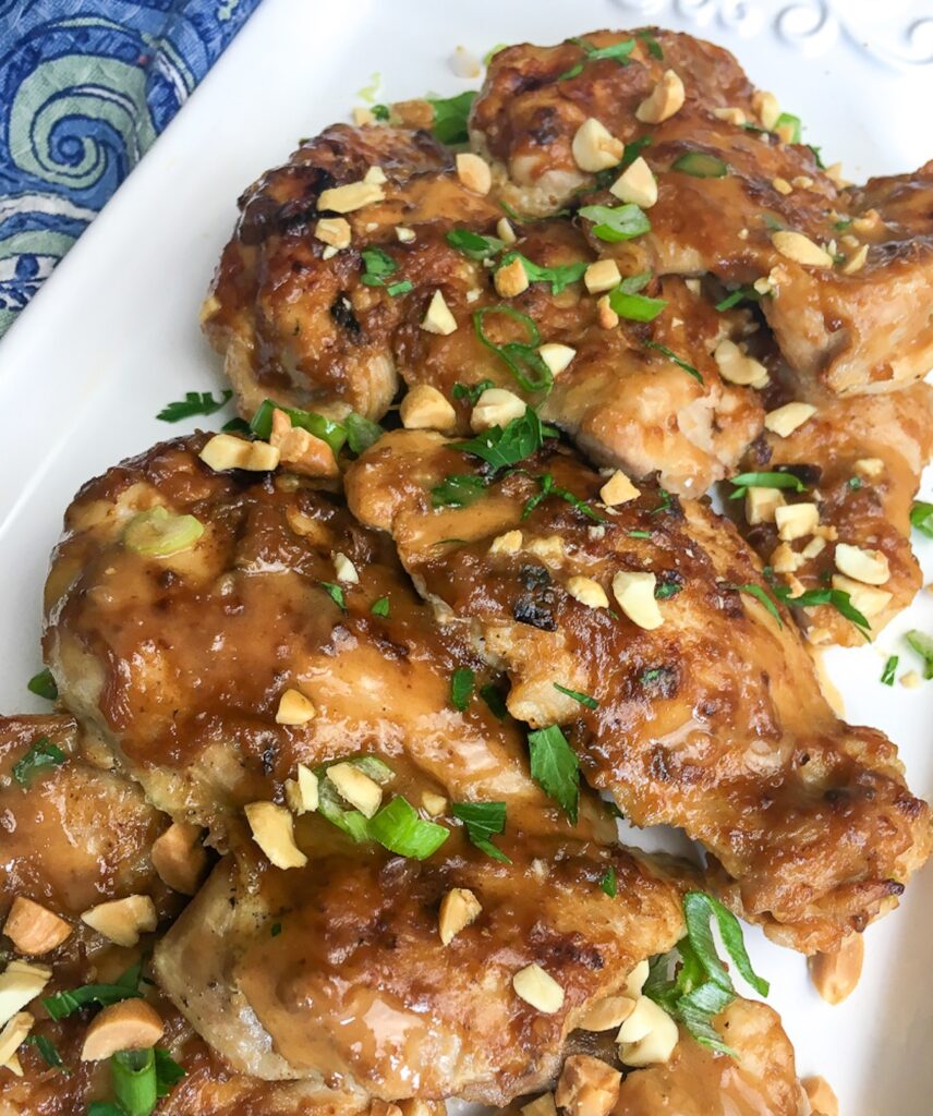 Platter of Thai chicken thighs garnished with peanuts and chopped onions.