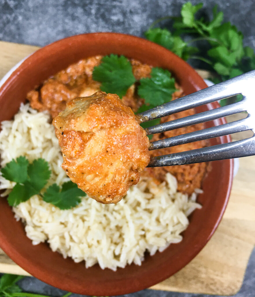 Fork with bite of chicken from Instant Pot tiki masala from Flavor Portal recipe with rice in a brown ceramic bowl on a wood platter