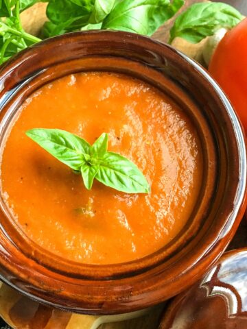 Instant Pot tomato basil soup in stoneware bowl with fresh tomatoes and basil on a wooden board