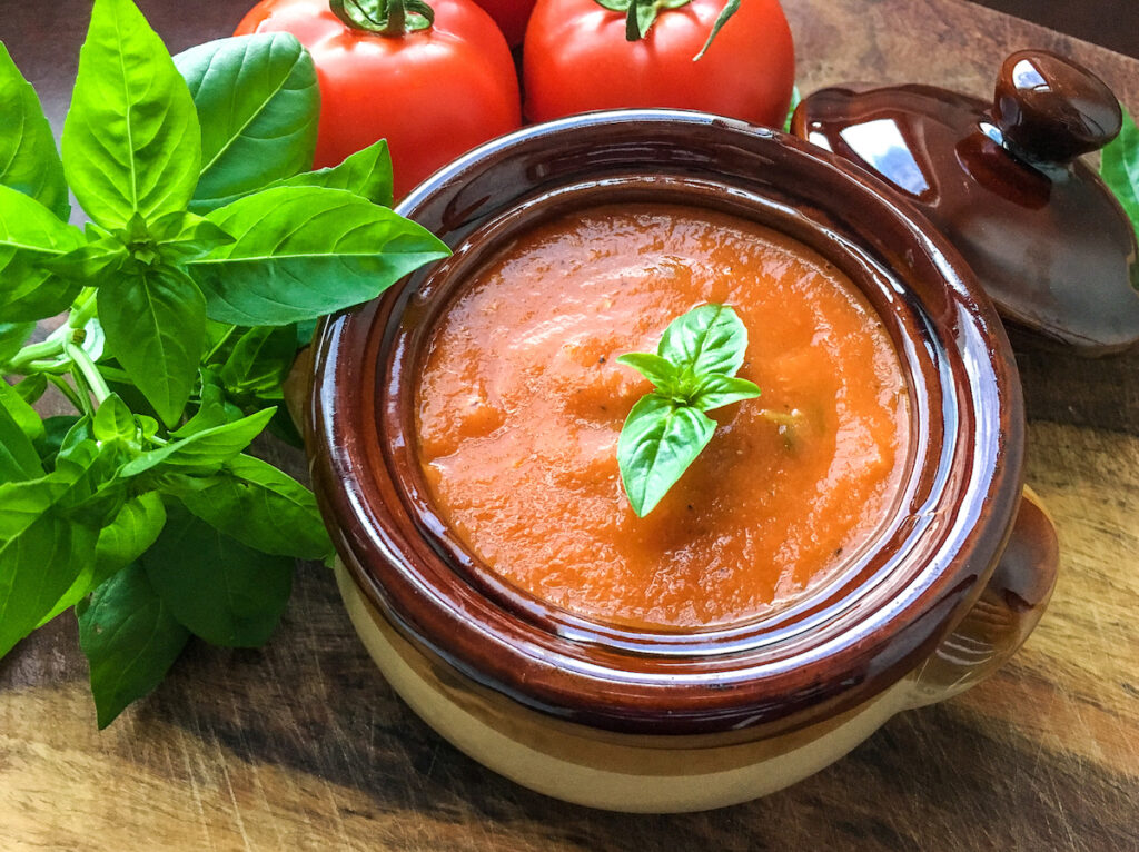 Instant Pot tomato basil soup in stoneware bowl with fresh tomatoes and basil on a wooden board