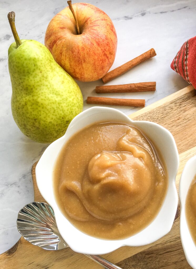 Instant Pot cinnamon pear applesauce in white 5 petal shape bowl with pear, apple and cinnamon sticks
