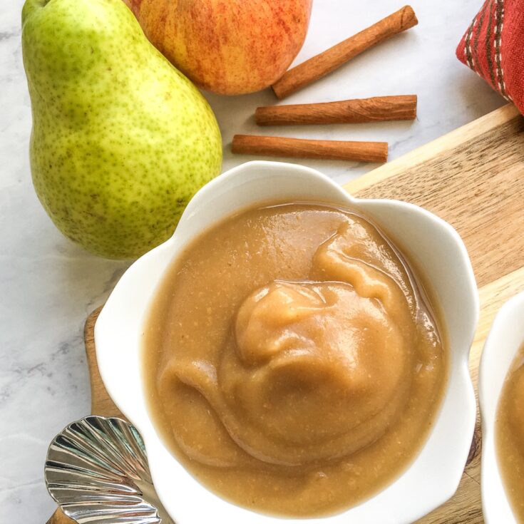 Instant Pot cinnamon pear applesauce in white 5 petal shape bowl with pear, apple and cinnamon sticks