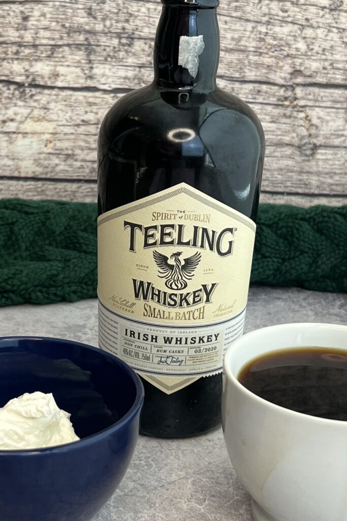 Irish whiskey bottle, cup of hot coffee and small blue bowl with whipped cream