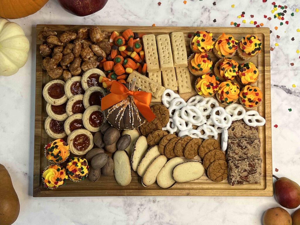 fall colored cookies, candies, nuts and cupcakes on a charcuterie board