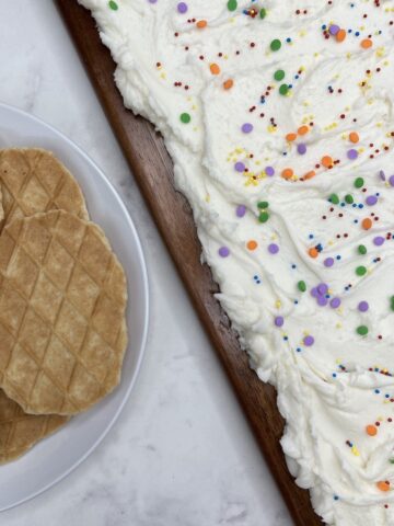 closeup of buttercream frosting board with rainbow sprinkles next to a plate of waffle crackers